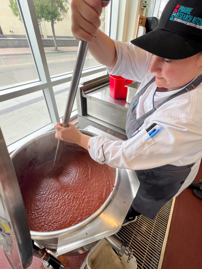 a person stirring a large pot of sauce