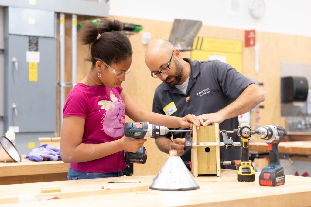 A young girl and an instructor working on a carpentry project together.