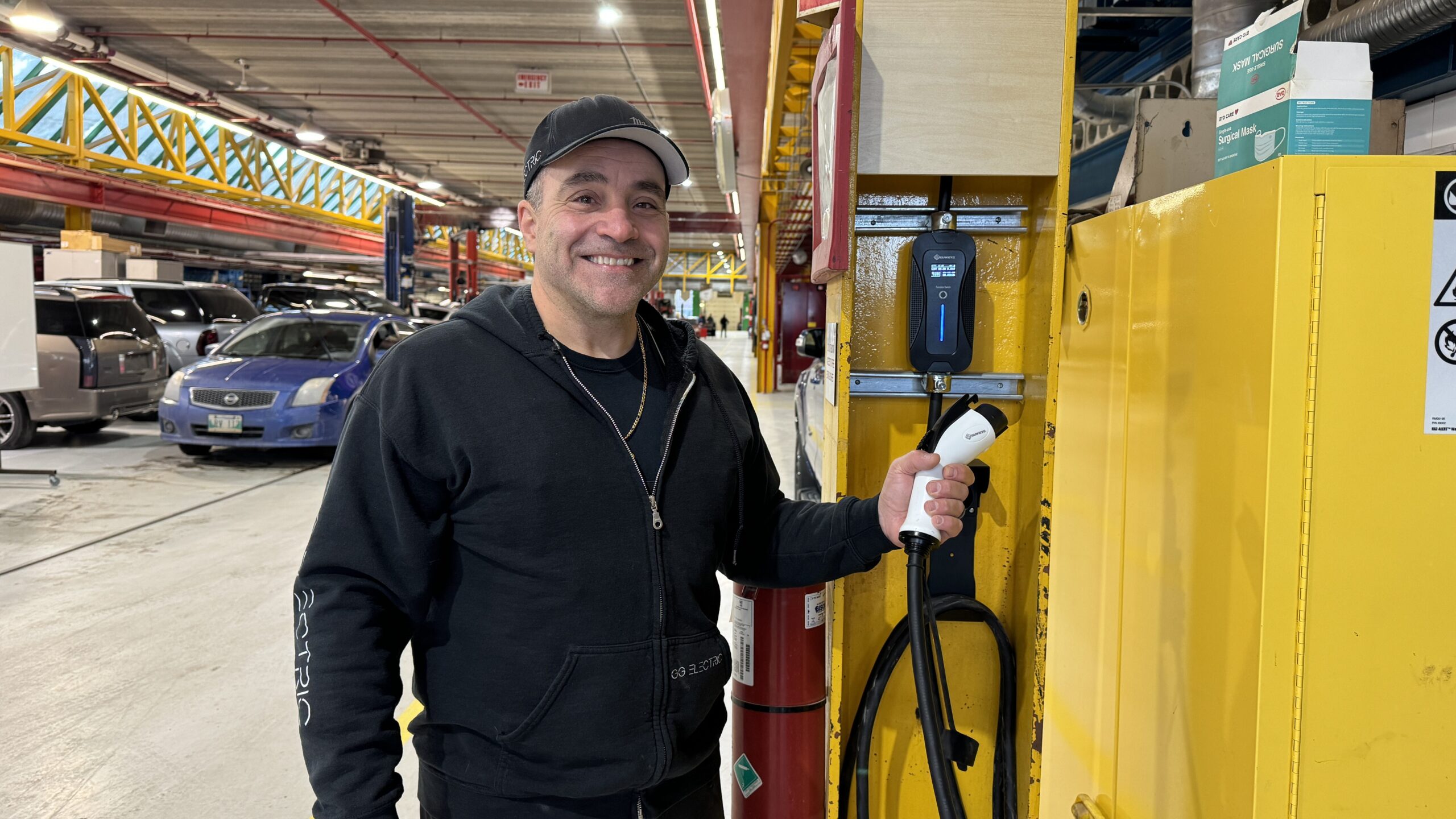 Greg stands smiling beside and electric vehicle charger.