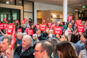 Audience members hold up thank-you signs at event announcing RRC Polytech as the home of the Schroeder Institute of Entertainment and Media Arts.