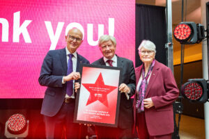 Walter and Maria Schroeder, with RRC Polytech President Fred Meier, holding a thank-you plaque at event announcing RRC Polytech as the home of the new Schroeder Institute of Entertainment and Media Arts.