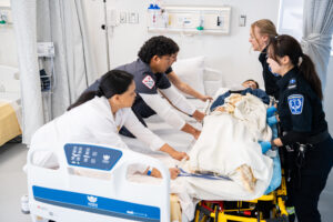 Nursing and Paramedicine students lifting a patient from stretcher to bed in RRC Polytech's Interdisciplinary Health and Community Services Simulation Centre.