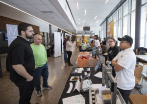 Two male guests visiting the Prairie Research Kitchen's booth at RRC Polytech's Research Partnerships & Innovation expo.