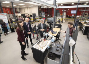 Group of men and women observing a robotics-controlled chess game.