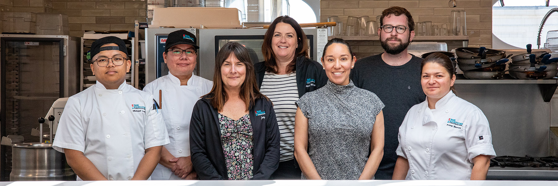 Group photo of seven people standing in a culinary lab