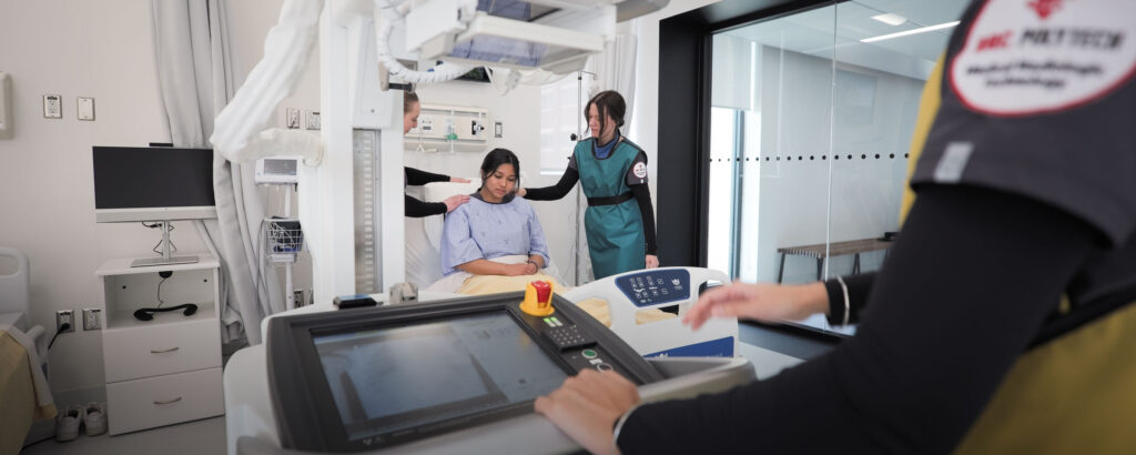 Medical radiology students simulate a procedure with a patient in a clinical lab setting.