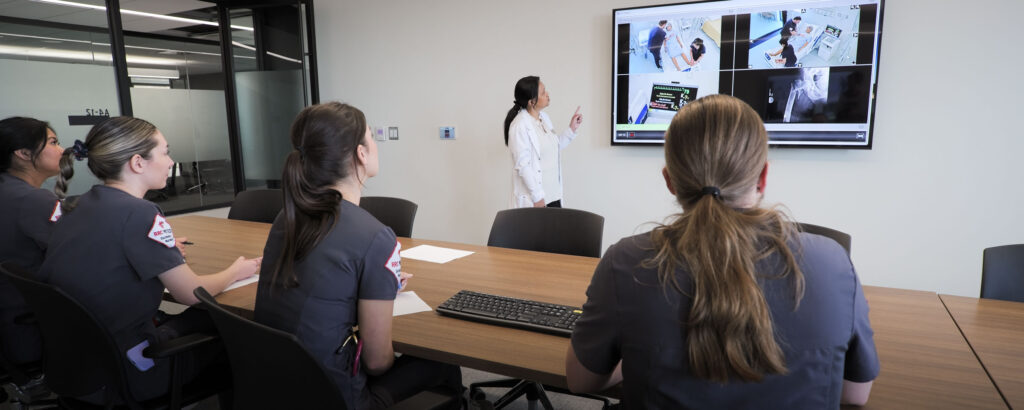 Nursing students in a classroom setting, viewing information on a screen.