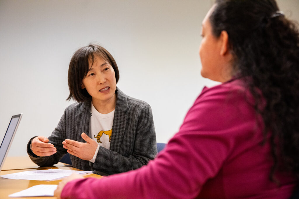 East Asian woman speaking to another woman in a classroom setting.