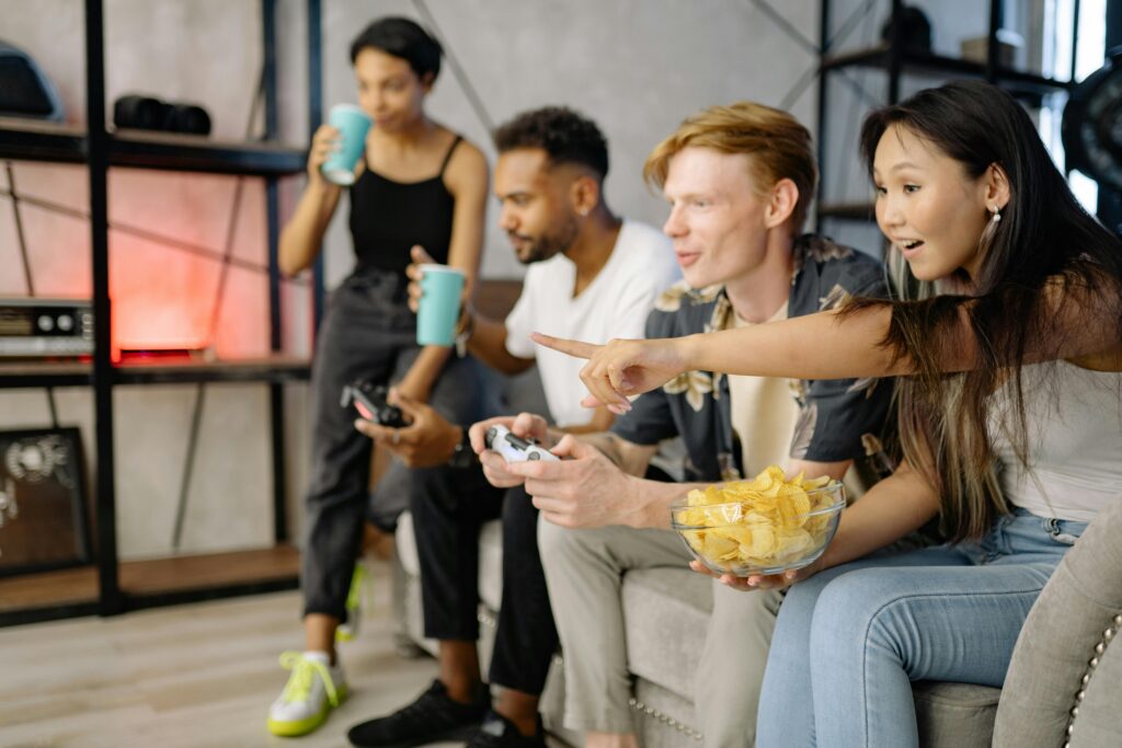 Friends sitting on a couch playing video games and eating snacks.