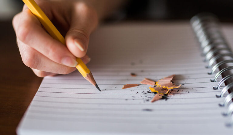 A hand writing in pencil on a piece of lined paper.