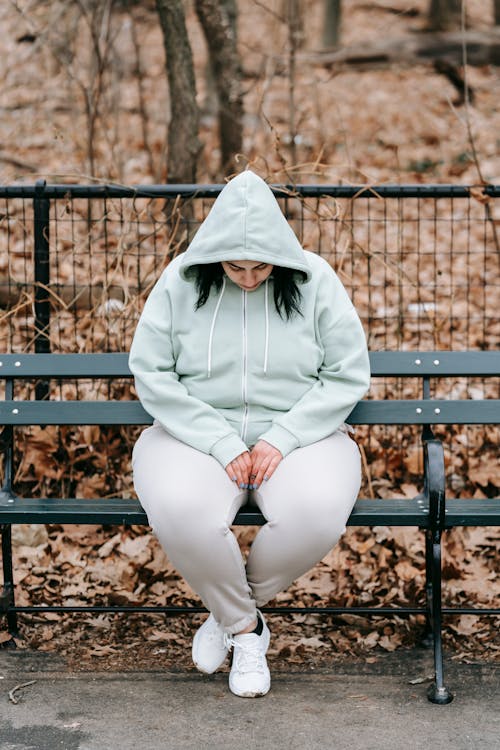 Woman sitting on park bench with head downcast