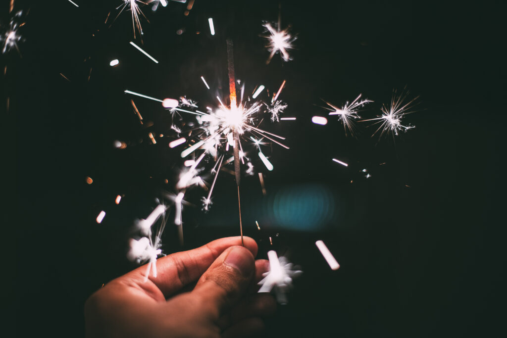 A hand holding a lit sparkler in the dark.