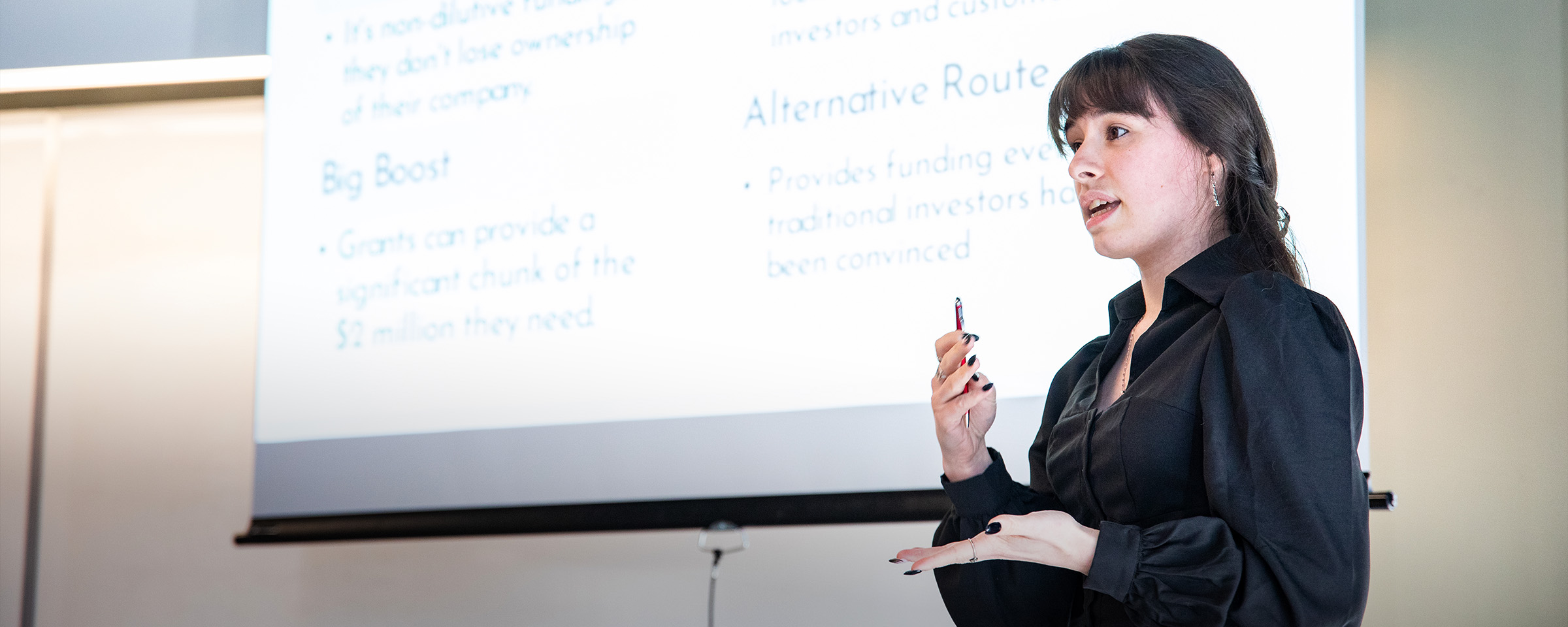 Female student making classroom presentation in front of projection screen.