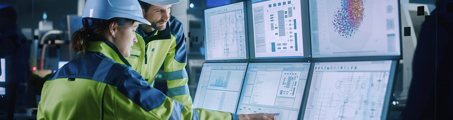 Man and woman looking at a wall of monitors and pointing to something on the screen