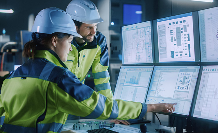 Man and woman looking at a wall of monitors and pointing to something on the screen