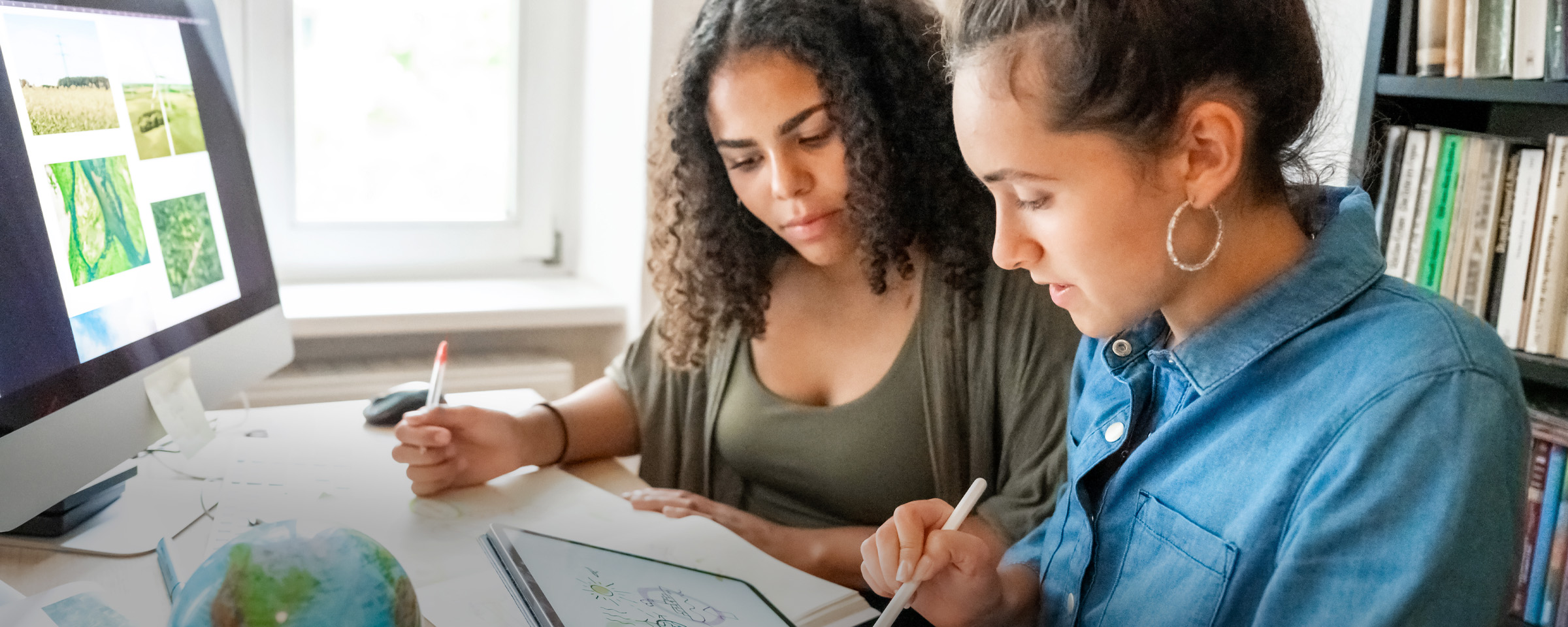 Two female students looking at images of greenspace and environmental imagery on desktop computer and tablet.